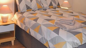 Un lit bien fait, recouvert d’une couvre-lit à motifs géométriques, avec deux lampes de chevet et une serviette pliée posée sur le lit.