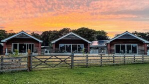 A row of three wooden cabins with large windows, a wooden fence in front, and a grassy field. - An ideal destination for relaxation, comfort, and immersion in nature’s beauty. (Old Buckenham)