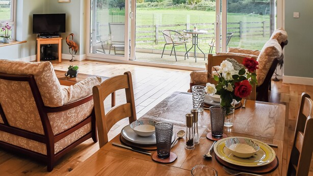 A dining area with a table set for four, a television, and a view of a fenced outdoor area. - An ideal destination for relaxation, comfort, and immersion in nature’s beauty. (Old Buckenham)
