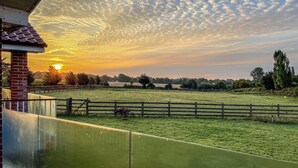 A sunset over a grassy field with a wooden fence and a brick building. - An ideal destination for relaxation, comfort, and immersion in nature’s beauty. (Old Buckenham)
