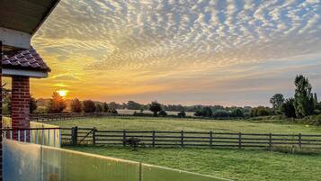 A sunset over a grassy field with a wooden fence and a brick building.