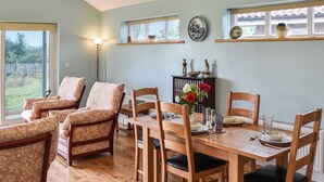 A dining area with a wooden table and chairs, a vase with flowers, and a view of the outdoors through large windows. - An ideal destination for relaxation, comfort, and immersion in nature’s beauty. (Old Buckenham)