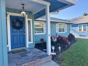 A house with a blue door, a front porch, and a small garden with poinsettias.
