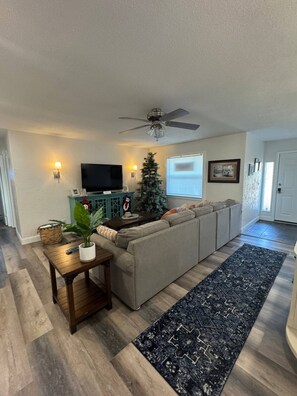 A living room with a sofa, a TV, a ceiling fan, a Christmas tree, and a patterned rug.