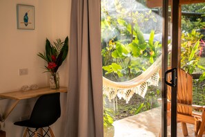 Une pièce comprenant un bureau, une chaise et donnant sur un jardin grâce à une porte vitrée.