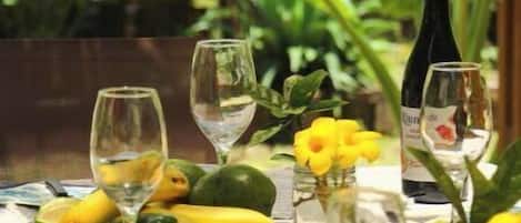 A table set with plates, glasses, and a bottle of wine, surrounded by tropical plants.