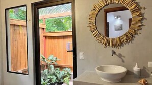 A bathroom with a wooden door, a mirror with a unique frame, a white sink, and a small plant on the counter. - Feeling Trees Jungle Lodge- Casa Pájaros (Provincia de Puntarenas)