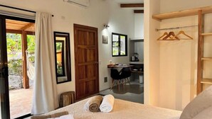 A bedroom with a bed, a wooden door, a desk with a chair, and a small kitchenette. - Feeling Trees Jungle Lodge- Casa Pájaros (Provincia de Puntarenas)