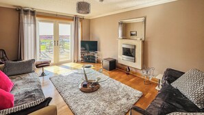 A modern living room with a sofa, a coffee table, a fireplace, and a television. - 2 bedroom accommodation in Gramsdale, Isle of Benbecula (Gramsdale, Isle of Benbecula)