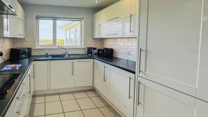 A modern kitchen with white cabinets, a black countertop, and a tiled floor. - 2 bedroom accommodation in Gramsdale, Isle of Benbecula (Gramsdale, Isle of Benbecula)