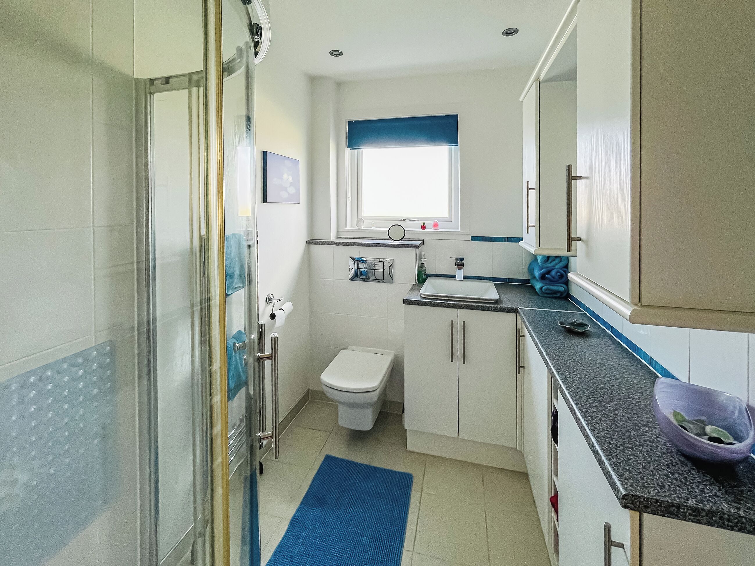 A compact bathroom with a shower, toilet, sink, and a small window.