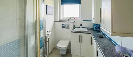 A compact bathroom with a shower, toilet, sink, and a small window.