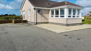 A two-story house with a tiled roof, a covered porch, and a satellite dish. - 2 bedroom accommodation in Gramsdale, Isle of Benbecula (Gramsdale, Isle of Benbecula)