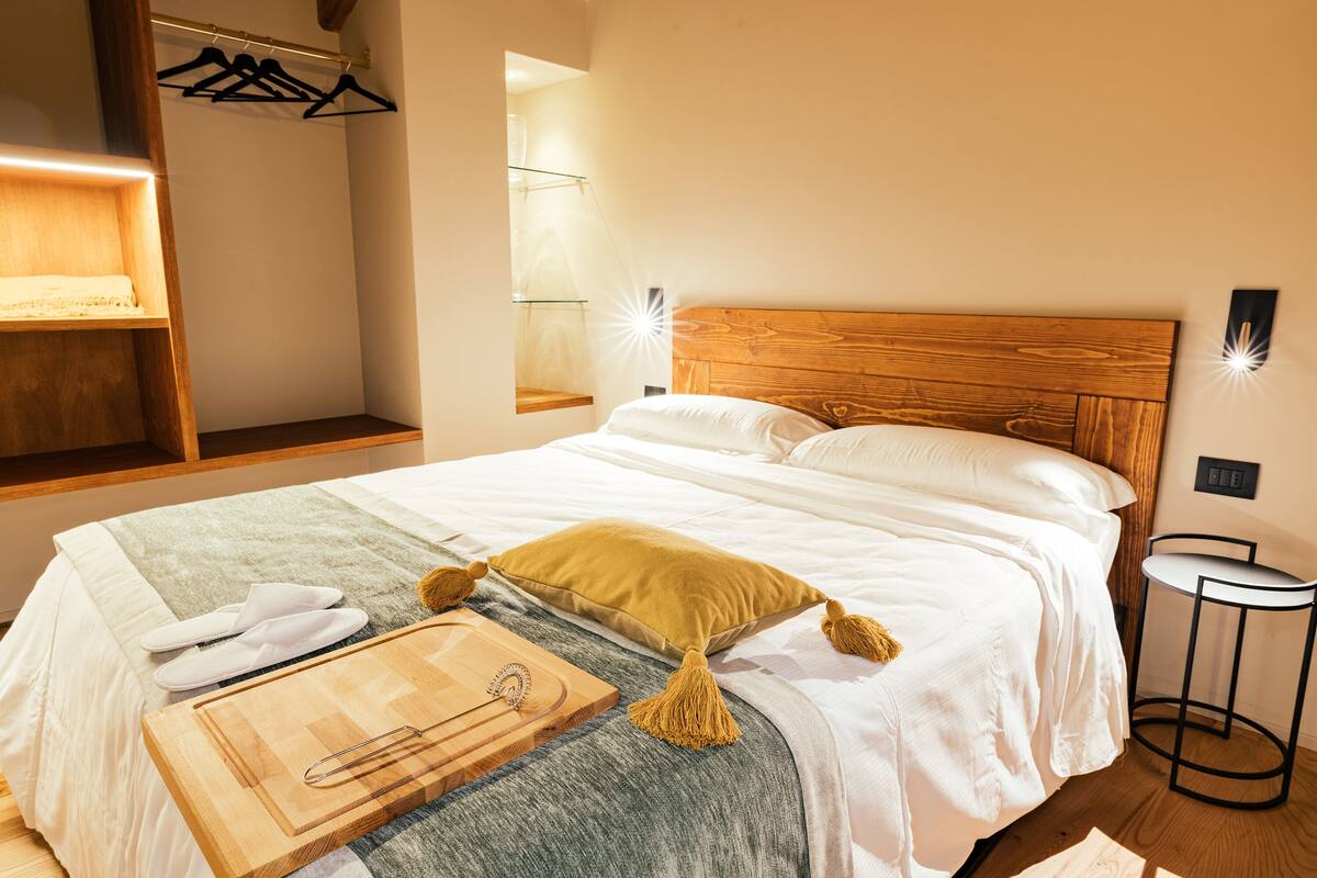 Ein ordentlich bezogenes Bett mit Holz Kopfteil, einem Nachttisch und einem an der Wand befestigten Kleiderhaken.
