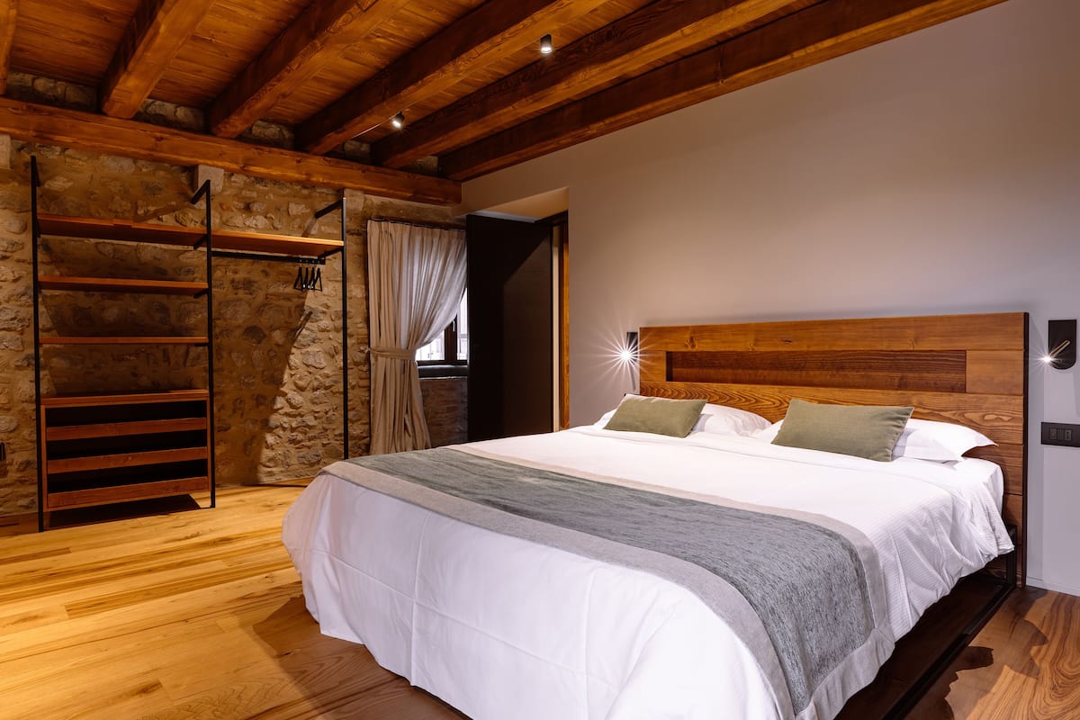 Ein Schlafzimmer mit Holzboden, Steinwänden, einem Bett mit weißer Bettwäsche und einem Holz-Kopfteil.