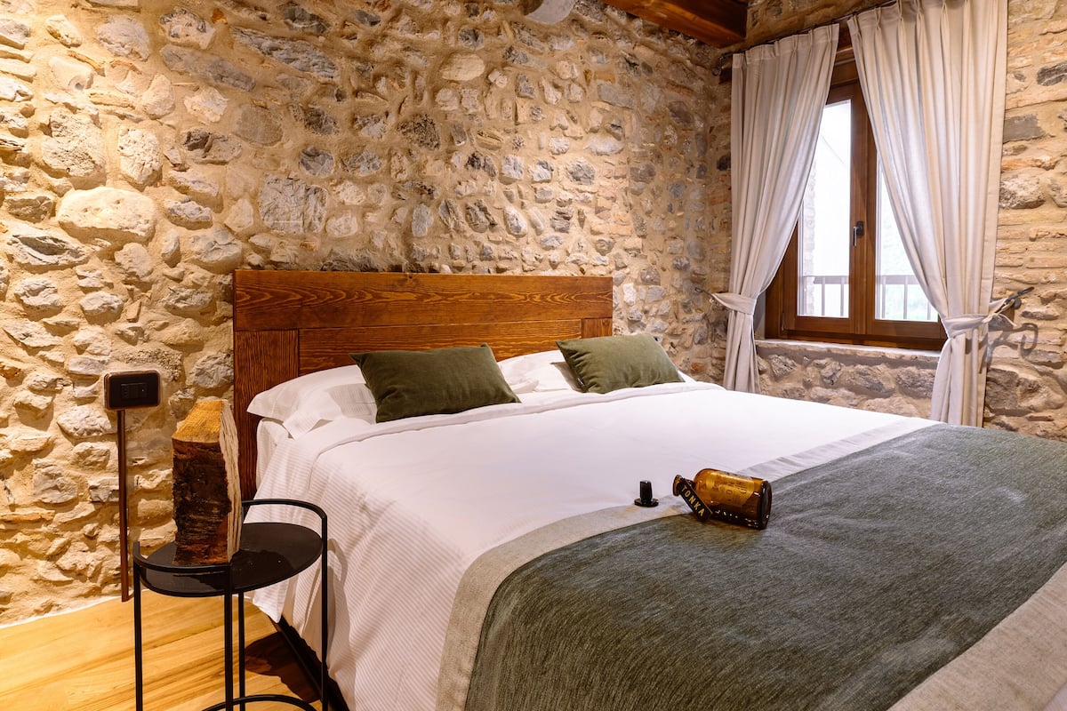 Ein Schlafzimmer mit einer Steinswand, einem hölzernen Bettgestell, weißer Bettwäsche und einer grünen Tagesdecke.