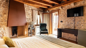 A bedroom with a stone wall, wooden beams, a fireplace, a bed with pillows, a chair, and a TV. - Casa del Vicario (Fagagna)