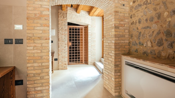 A hallway with exposed brick walls, a wooden door with a grid pattern, and a white air conditioning unit. - Casa del Vicario (Fagagna)