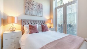 A bedroom with a large bed, two bedside tables with lamps, a window with blinds, and a painting on the wall. - 2 bedroom accommodation in Hexham (Hexham)