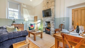 A cozy living room with a stone fireplace, a flat-screen TV, a sofa, and a dining table set for two. - 2 bedroom accommodation in Hexham (Hexham)