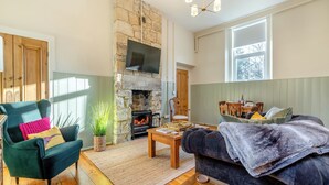 A cozy living room with a stone fireplace, a comfortable sofa, a wooden coffee table, and a television mounted on the wall. - 2 bedroom accommodation in Hexham (Hexham)