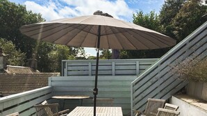 Eine Holzterrasse mit Tisch und Stühlen, einem großen Sonnenschirm und einer Treppe.