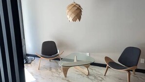 A modern room with a glass coffee table, two chairs, and a unique woven pendant light.