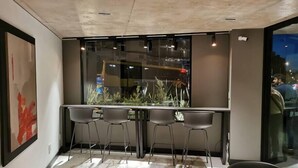 A modern dining area with a long table, four chairs, and a window with a view of the city at night.