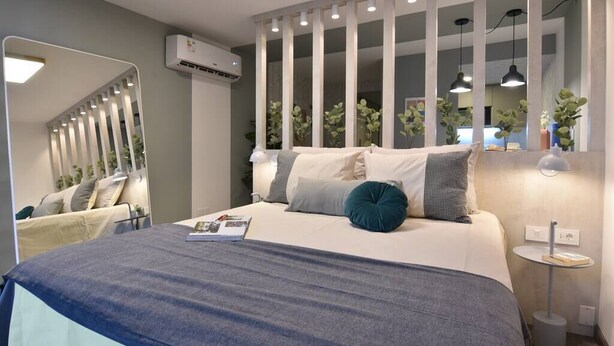 A modern bedroom with a large bed, a mirror, and a small bedside table with a lamp.