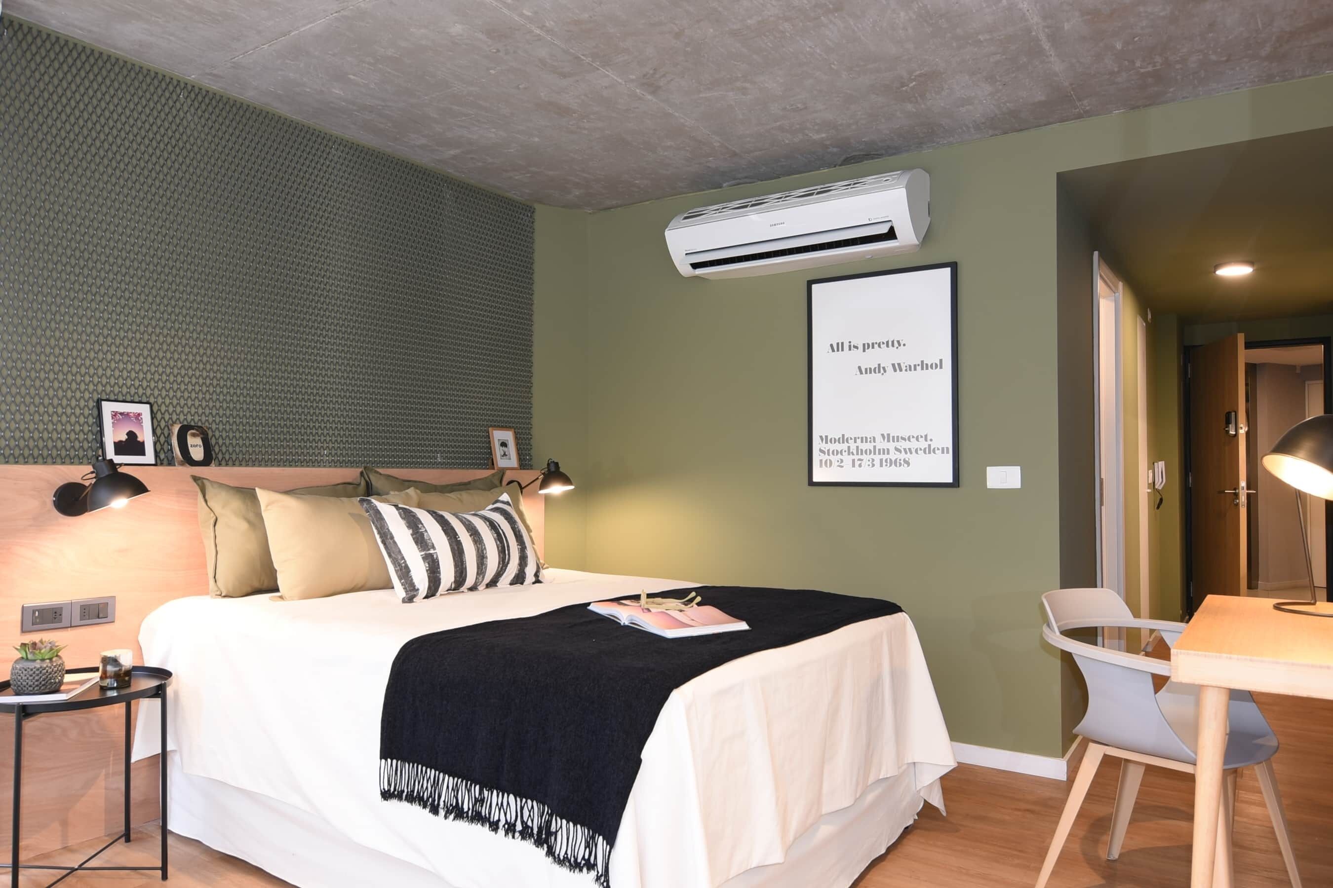 Et moderne hotelværelse med en stor seng, sengeborde med lamper, et skrivebord og et indramet citat på væggen.