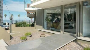 Een modern gebouw met een glazen gevel, een terras en uitzicht op de straat.