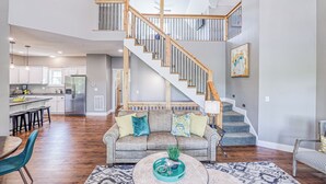 A spacious living area with a wooden staircase, a sofa with cushions, and a dining table.