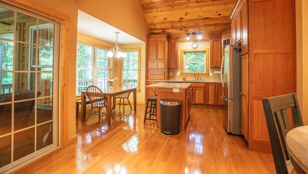A spacious kitchen with wooden cabinets, a stainless steel refrigerator, and a dining area with a table and chairs. - Redbud Retreat ~ Rustic family friendly cabin with New Hot Tub in Townsend! (Townsend)
