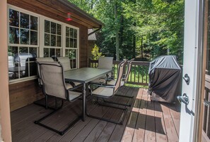 An outdoor deck with a table and chairs, a barbecue grill, and a wooden cabin in the background. - Redbud Retreat ~ Rustic family friendly cabin with New Hot Tub in Townsend! (Townsend)