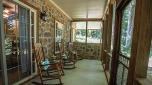 A covered porch with stone walls, wooden rocking chairs, and a view of the forest. - Redbud Retreat ~ Rustic family friendly cabin with New Hot Tub in Townsend! (Townsend)