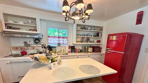 Une cuisine avec des meubles blancs, un réfrigérateur rouge et une fenêtre ornée d’une pancarte indiquant « RELAX ».