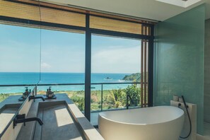 A modern bathroom with a large bathtub, a sink with two faucets, and a view of the ocean.