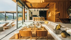 Um interior moderno com um amplo painel de vidro, teto de madeira e uma área de jantar com mesa e cadeiras.