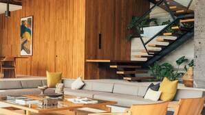 Uma sala de estar moderna com parede de madeira, uma mesa de centro de vidro, um sofá e uma escada com guarda-corpo de vidro.