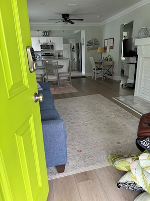 Une pièce avec une porte vert vif, un canapé bleu, un tapis à motifs, un pouf marron et un téléviseur dans un coin.