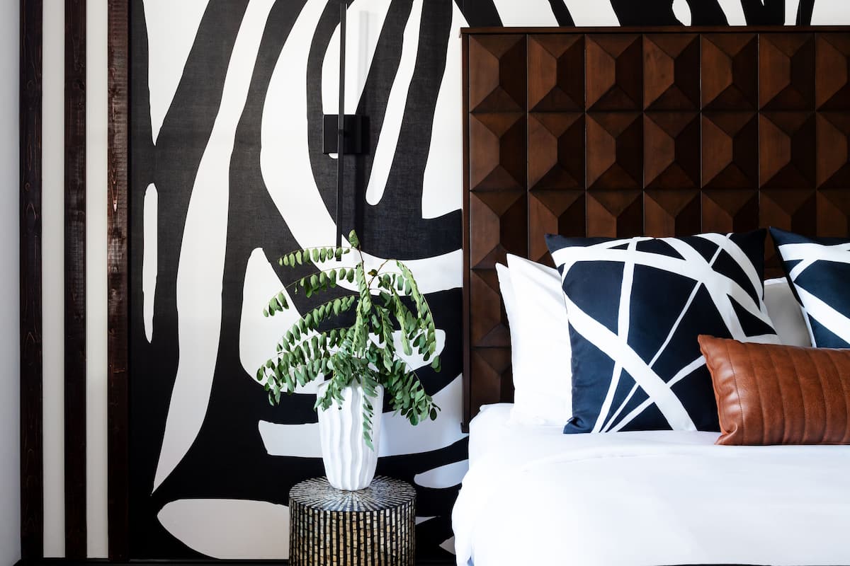 A modern bedroom with a large abstract wall art, a wooden headboard, and a bedside plant.