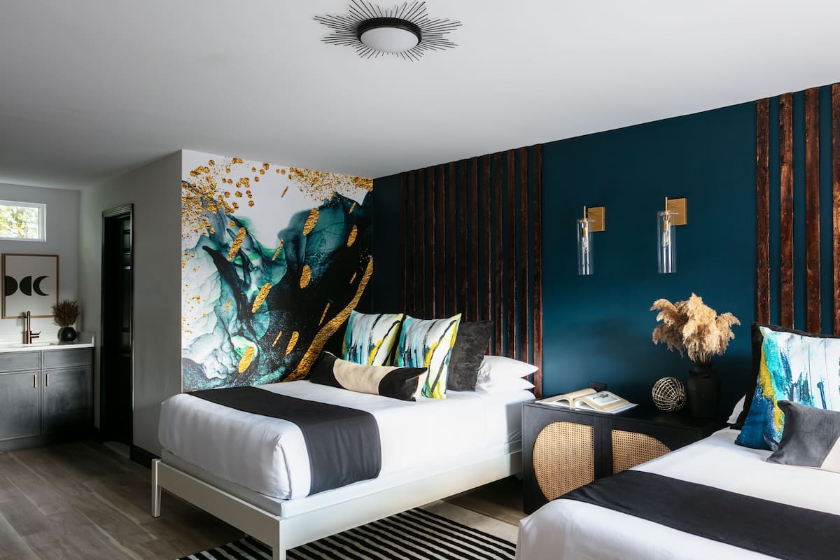 A modern hotel room with two beds, a large abstract painting on the wall, and a dark blue accent wall.