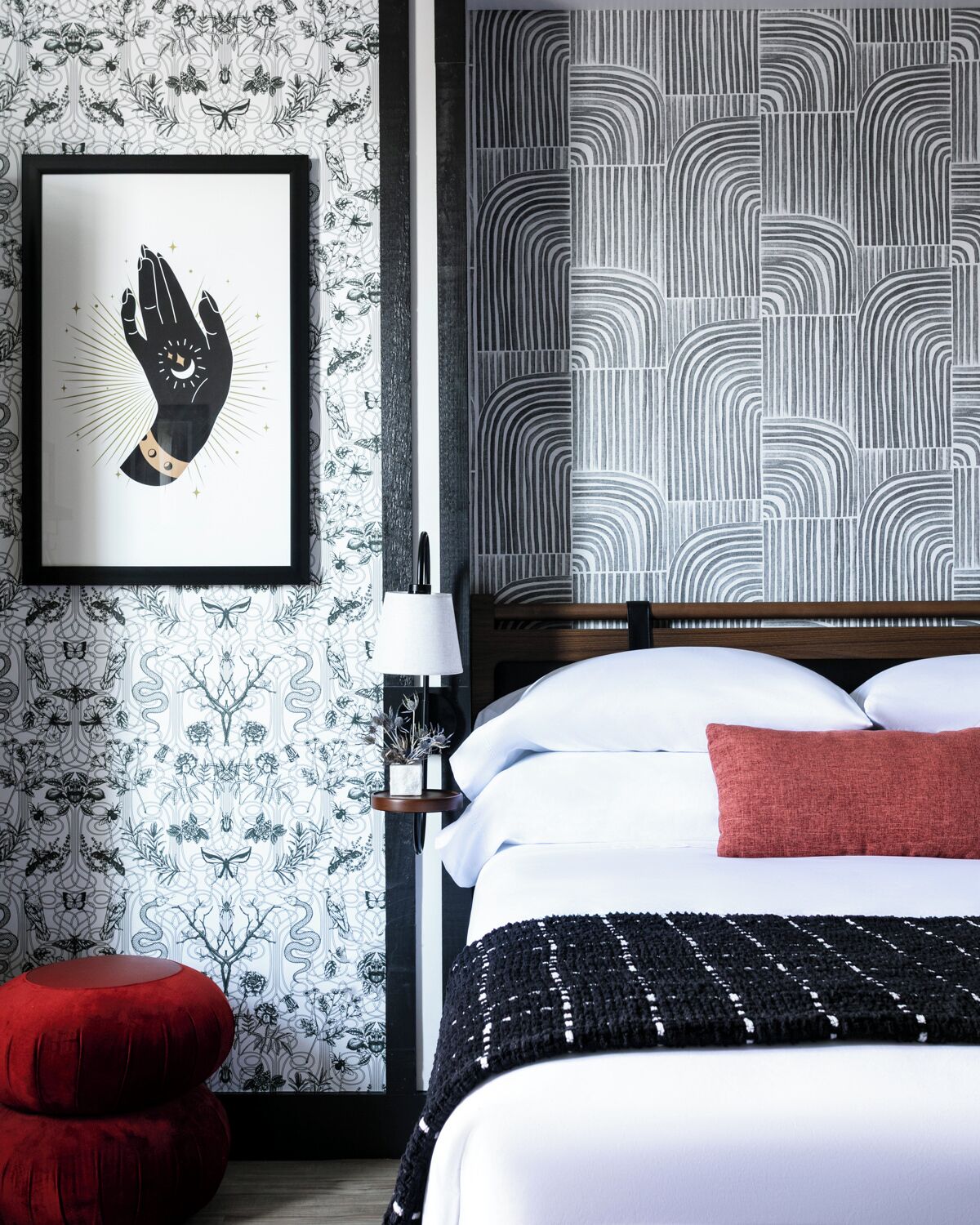 A hotel room with a bed, a red chair, a framed artwork, and a patterned wall.