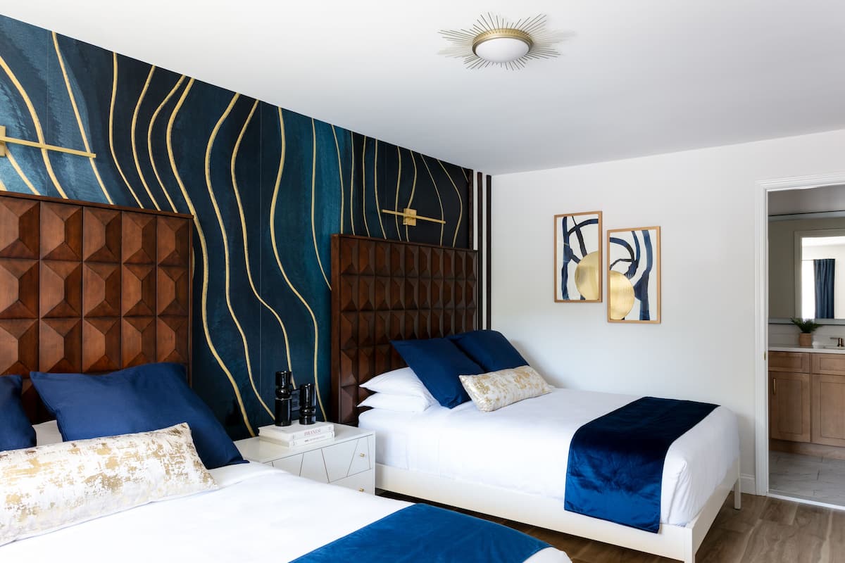 A hotel room with two beds, a geometric-patterned headboard, abstract wall art, and a visible bathroom.