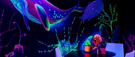 A room with a glowing whale sculpture, a table with a vase, and two white chairs.