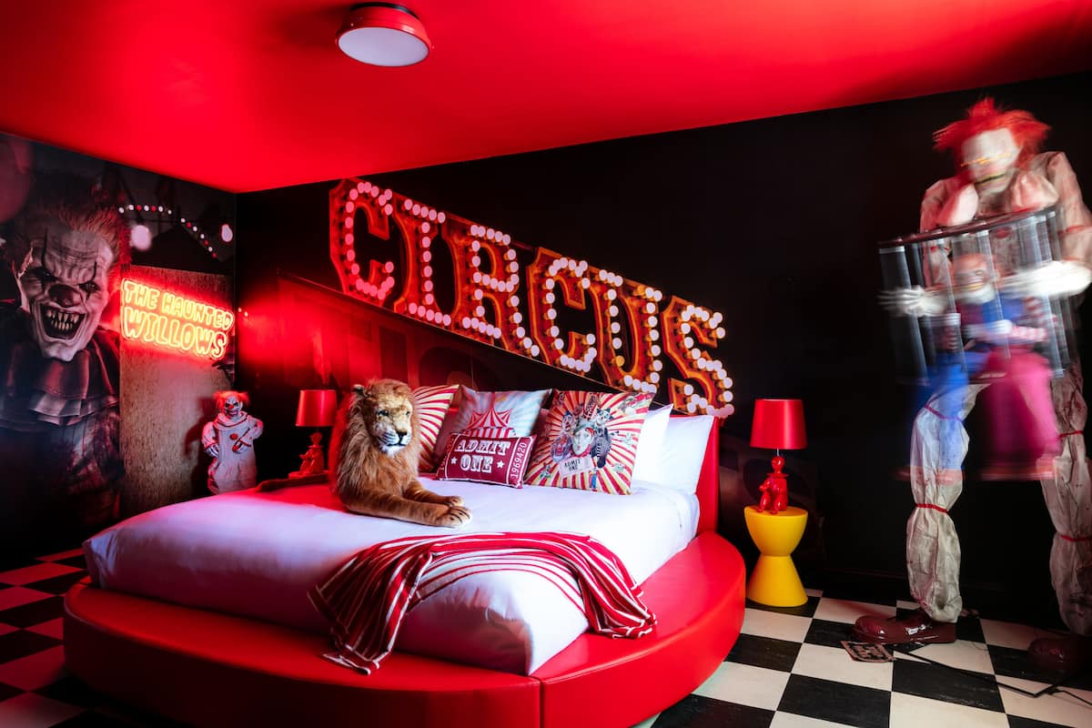 A red-themed bedroom with a lion statue on the bed, circus-themed decorations, and a neon sign.