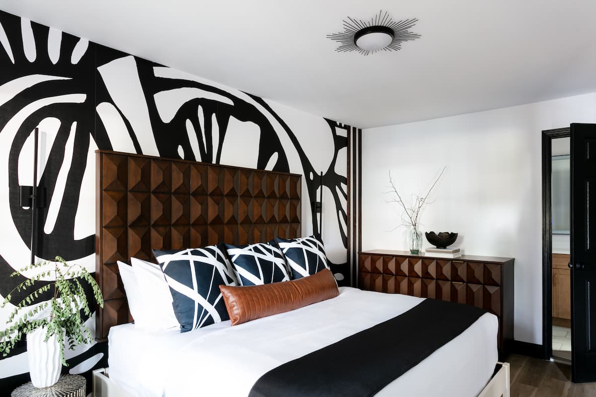 A modern bedroom with a geometric-patterned headboard, a white bed, and a decorative wall piece.
