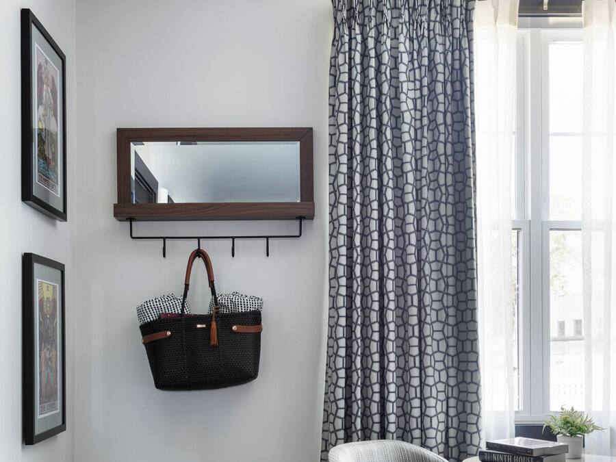 Een moderne kamer met een houten vloer, een zwart-wit gordijn, een houten stoel, een klein rond tafeltje met een plant erop en een spiegel aan de muur.