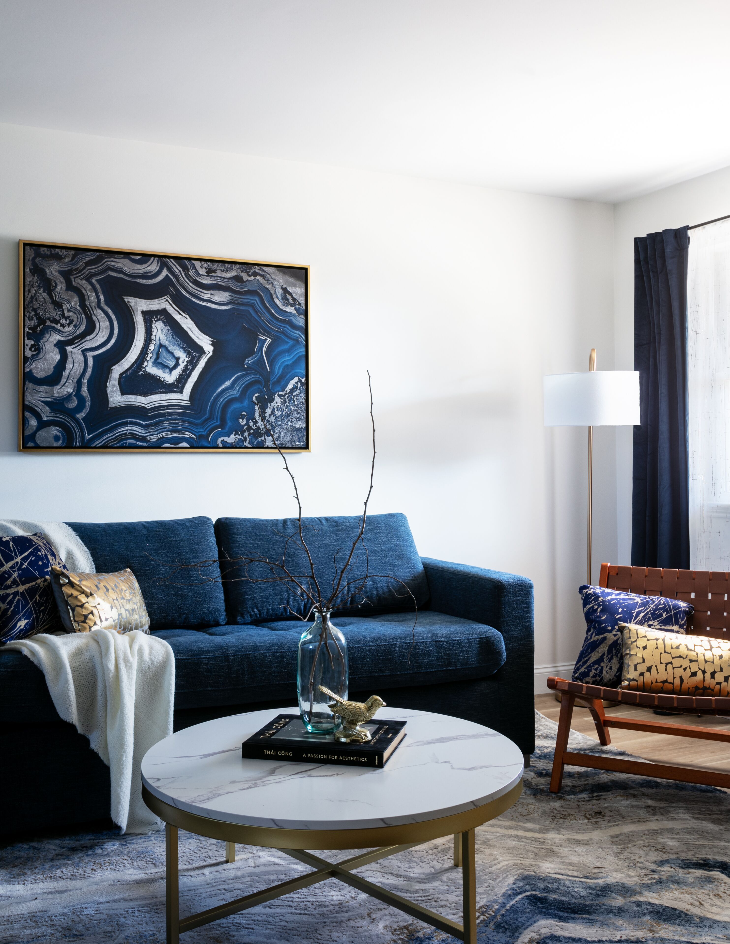 Una sala de estar moderna con un sofá azul, una mesa de centro redonda y un cuadro abstracto grande en la pared.