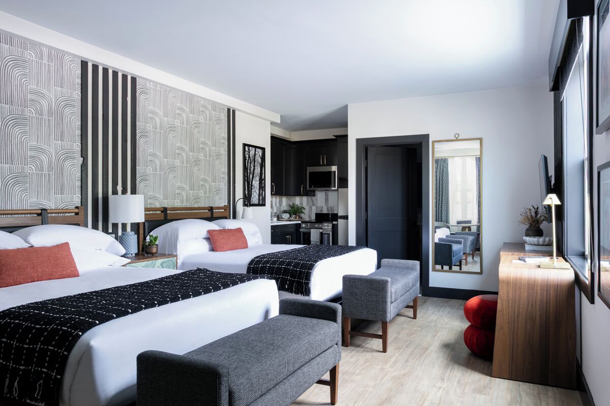 Una camera d'albergo moderna con due letti, un'area salotto, un angolo cottura e un bagno.
